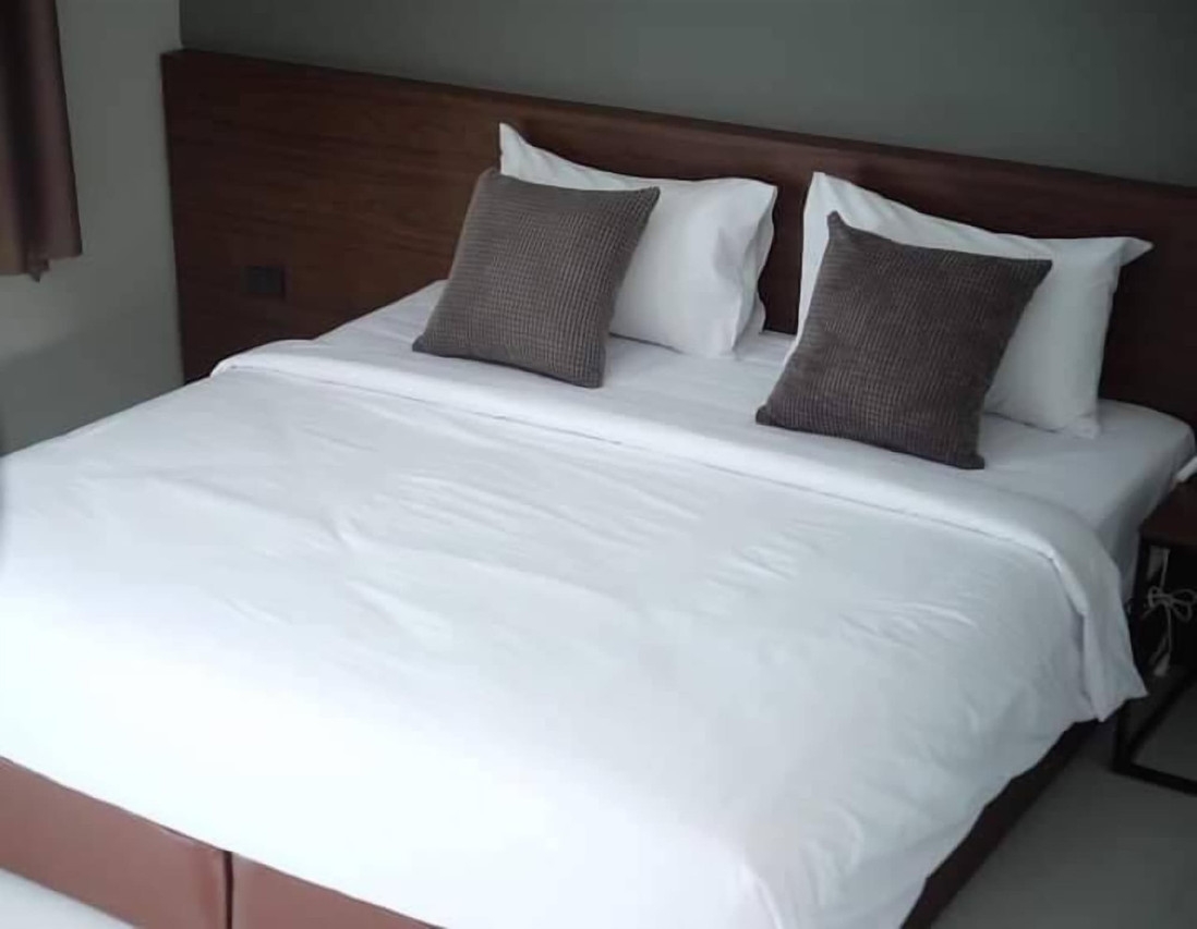 Bedroom with a large bed, dark wood headboard, white linens and brown cushions in a calm grey palette